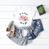 Do No Harm Take No Shit Floral Sublimation Transfer, a white T-shirt with a colorful floral design and bold text, paired with striped skirt, distressed jeans, gray shoes, and a small plant on a white wooden surface.