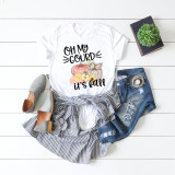 Oh My Gourd It's Fall Sublimation Transfer, a fall-themed white t-shirt with pumpkin and sunflower design and playful text, displayed alongside denim shorts, striped skirt, gray shoes, a plant, and a book on a white wooden background.