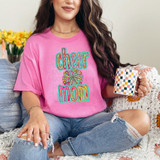 Cheer Mom Glitz DTF Heat Transfer, pink T-shirt with colorful cheer mom design and fireworks, worn by a woman sitting on a cozy blanket holding a patterned mug.