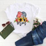 Cheer Mom Sunflower Floral Sublimation Transfer, showcasing a t-shirt with a colorful sunflower and floral design with the word Mom, on a flat lay with sunglasses, a green wallet, pink flowers, and jeans.