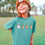 Easter Pac DTF Heat Transfer, cute cartoon bunny and carrot design on a child's teal T-shirt outdoors.