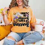 Don't Be Stressing Life's A Blessing DTF Heat Transfer, colorful floral design and uplifting quote on a woman's orange T-shirt.