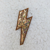 BRONZE Sequin Lightning Bolt HAT/POCKET Patch, a decorative patch with a lightning bolt shape embellished with shiny bronze sequins and a bronze embroidered border, on a light textured background.