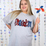 Freedom Doodle DTF Heat Transfer, woman wearing a graphic t-shirt with patriotic heart and American flag design, smiling and holding a patriotic pinwheel, with a shiny star-shaped decorations background.