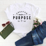 Cross Religious Sublimation Transfer, white T-shirt with quote 'Created With a Purpose' and a small cross design, arranged with green wallet, sunglasses, blue jeans, and flowers on a white surface.
