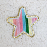 Multicolored Star Embroidered & Glitter HAT/POCKET Patch, a colorful star-shaped patch with rainbow-colored embroidery and a gold glitter border on a light textured background.