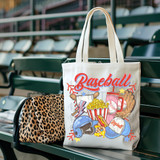 Baseball Muted Collage DTF Heat Transfer, tote bag with baseball-themed illustrations and text, resting on a green bench alongside a leopard-print bag.