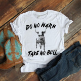 Do No Harm Take No Bull Sublimation Transfer, white t-shirt with a black bull graphic and bold text, paired with cowboy boots and jeans, on a wooden surface.