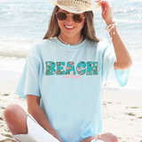 Beach Vibes DTF Heat Transfer, colorful beach-themed lettering design on a light blue T-shirt worn by a woman at the beach.