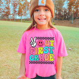 Peace Out First Grade DTF Heat Transfer, vibrant graphic design with a peace sign, smiley face, and colorful text on a pink t-shirt worn by a young girl in an outdoor park setting.
