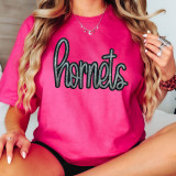 Hornets Sequin Patch, close-up view of a pink T-shirt with a black and silver sequined Hornets logo on the front worn by a woman with long blonde wavy hair, accessorized with jewelry.
