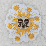 Sun Embroidered HAT/POCKET Patch, embroidered patch with a smiling sun face and floral designs in yellow, white, and black on white fabric background.