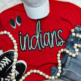 Indians Sequin Patch, vibrant red t-shirt with 'Indians' written in sequins, paired with denim shorts, black sneakers, a grey cap, big earrings, and a beaded necklace.