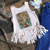 Leopard Cactus Sublimation Transfer, a white sleeveless top with fringe details and a leopard print cactus design, displayed on a rustic wooden surface with denim jeans, cowboy boots, and flowers.