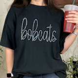 Bobcats Sequin Patch, close-up of a black T-shirt with a colorful, sparkly sequined 'bobcats' patch in cursive writing on the front.