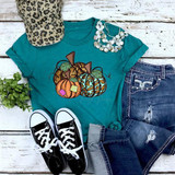 Leopard Patchwork Pumpkins Screen Print Heat Transfer, showcasing a teal t-shirt with pumpkin illustrations, paired with blue jeans, black sneakers, a leopard print cap, a white pearl necklace, and greenery on a rustic white wooden background.
