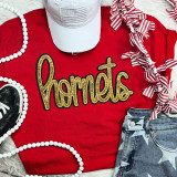 Hornets Gold Sequin Patch, a glittery gold sequin embroidered patch spelling 'hornets' on a red t-shirt