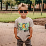Fifth Grade Rocks Blue/Green DTF Heat Transfer, colorful boy wearing sunglasses and a T-shirt with 'Fifth Grade Rocks' design at park.