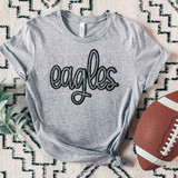 Eagles Faux Sequin Patch DTF Heat Transfer, grey t-shirt with sequin eagle patch design on front, laid on patterned surface near football and green leaves.