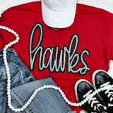 Hawks Sequin Patch, sparkling black and white sequin patch spelling 'Hawks' on a red t-shirt, casual outfit with denim jeans and black sneakers, accessorized with white beaded necklace and a white cap.