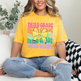 Third Grade Coquette Pencil Bow DTF Heat Transfer, colorful graphic design featuring a bow and text on a yellow T-shirt worn by a smiling woman.