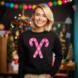 Pink Sequins Candy Canes Patch, close-up of a bright pink and white sequined candy canes patch on a black sweatshirt, worn by a smiling woman in a festive holiday setting with Christmas trees and colorful decorations in the background.