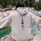 Moons DTF Heat Transfer, hoodie with moon and star design on the back, worn by person standing near a river and rocky landscape, outdoor scene.