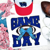 Royal Chenille Football Game Day with Sequin Bow (BLACK BACKING) Patch, close-up of a white shirt featuring a blue football with a blue sequin bow, surrounded by game day themed accessories.
