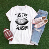 Tis the season Football Sublimation Transfer, a graphic T-shirt with a football design and text, casual sneakers, ripped jeans, and a football on green grass.