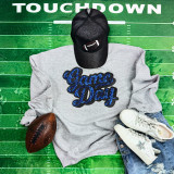 Royal Blue Sequins Game Day Patch, a sparkling blue sequins patch with the words 'Game Day' embroidered on a gray sweatshirt, paired with white sneakers, a black football cap, and a football on a green football field background.