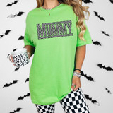 Mummy Checkered DTF Heat Transfer, a neon green T-shirt with a checkered 'MUMMY' graphic, worn by a woman holding a checkered mug against a spooky bat-decorated background.