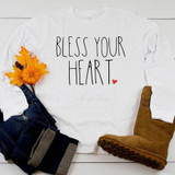 Bless your heart Sublimation Transfer, white sweatshirt with black text 'Bless your heart' and small red heart, surrounded by fall decorations including a small pumpkin, leaves, and a pair of brown boots.