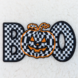 Checkerd BOO Embroidered HAT/POCKET Patch, Halloween-themed patch featuring a pumpkin with a checkered pattern face, orange embroidered outline, and black eyes and mouth.
