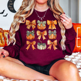 Vintage Pumpkin Coquette DTF Heat Transfer, a woman wearing a maroon sweatshirt with colorful pumpkin and bow designs perfect for autumn or Halloween celebrations.
