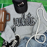 Jackets Sequin Patch, grey sweatshirt with black and white sequin patch saying 'jackets' on it, also includes black glitter cap with smiley face, brown tumbler with white percentage symbol, white beaded necklace, and casual jeans and sneakers, all laid out on a green surface.