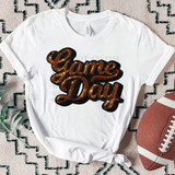 FAUX Orange Sequins Game Day Patch DTF Heat Transfer, image of a white T-shirt with orange sequin glitter text that says 'Game Day' in a cursive font, placed on a patterned rug next to a football.
