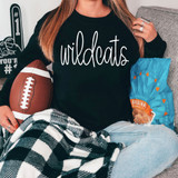 Wildcats Mascot WHITE DTF Heat Transfer, white text on black fabric shirt with girl sitting on sofa holding football and snack bag