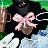 Sequin Football with Pink Sequin Bow Patch, fashion flat lay featuring a black sweatshirt with the sequin football and pink bow patch design, paired with white sneakers, blue jeans, a brown beverage tumbler, and white pearl necklaces on a green background.