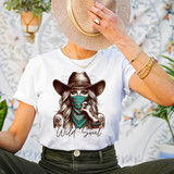 Wild Soul Cowgirl DTF Heat Transfer, Woman wearing a graphic T-shirt with a cowgirl illustration, cowboy hat, and bandana, in a casual and stylish setting.