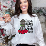 Life Is Better In A Small Town Christmas Water Tower DTF Heat Transfer, a woman wearing a white sweatshirt with Christmas water tower and poinsettia graphic design.