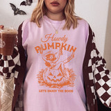 Howdy Pumpkin Pin Up ORANGE DTF Heat Transfer, vibrant orange graphic of a pin-up girl sitting inside a jack-o'-lantern with the text "Howdy Pumpkin" and "Let's Enjoy The Boos" on a light purple t-shirt.