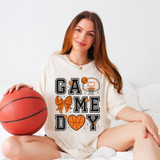 Game Day Basketball DTF Heat Transfer, young woman wearing a white T-shirt with basketball-themed graphic design, sitting on bed with basketball, indoor setting.