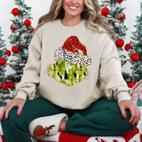Mean Guy Brushstroke DTF Heat Transfer, Christmas-themed sweatshirt with a Santa hat and abstract paint design on the front, worn by a smiling woman sitting cross-legged near Christmas trees.