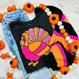 Pink Sequin Turkey Patch, colorful felt turkey patch with sequins on black fabric, paired with blue denim jeans and a black, orange, pink, and purple striped sweater, decorated with a pumpkin garland.