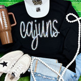 Cajuns Sequin Patch, sparkling multicolored sequin patch spelling 'Cajuns' on a black fabric surface.