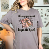 Always Put Your Hope In God DTF Heat Transfer, a woman wearing a T-shirt with religious design and text in a cozy indoor setting.