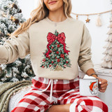 Faux Embroidery Coquette Christmas Tree DTF Heat Transfer, Christmas tree design with red bow, poinsettias, and ornaments on a beige sweatshirt worn by a woman with holiday decorations in the background.