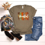 Thankful Brushstrokes Screen Print Heat Transfer T-shirt with autumn-colored brushstrokes and cursive 'Thankful' text, styled with ripped jeans, plaid scarf, black ankle boots, and dried floral bouquet on white wooden background.
