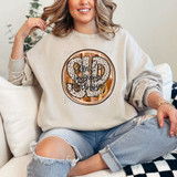 SLP Fall Brushstrokes DTF Heat Transfer, a woman wearing a beige sweatshirt with a colorful graphic design and text, sitting on a white sofa.