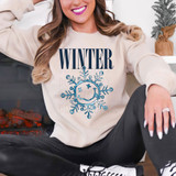 Winter Happy Face Snowflake DTF Heat Transfer, a blue snowflake with a smiling face and the word 'WINTER' in bold letters on a woman's sweatshirt.